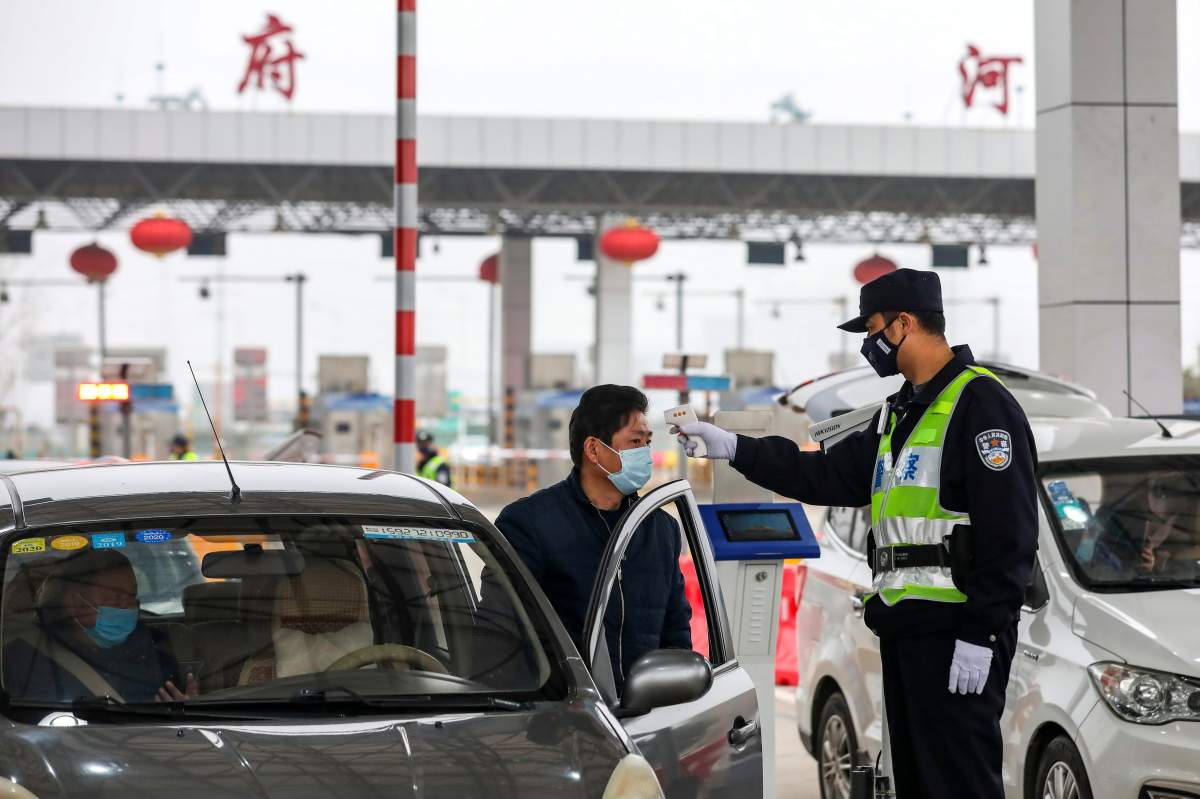 FILE – In this Jan. 23, 2020, file photo, a policeman uses a digital thermometer to take a driver’s temperature at a checkpoint at a highway toll gate in Wuhan in central China’s Hubei Province.
