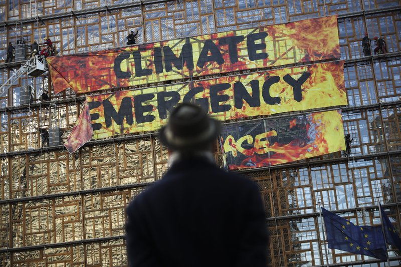 FILE - In this file photo dated Thursday, Dec. 12, 2019, a man looks up as police and fire personnel move in to remove climate activists and their banner, after they climbed the Europa building during a demonstration outside an EU summit meeting in Brussels.