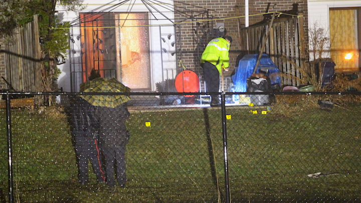 An officer places evidence markers on the ground behind an east-end Toronto home after a shooting early Saturday. A back door was damaged during the incident.