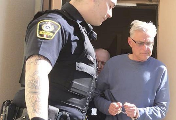 John Brittain is escorted from the RCMP detachment in Penticton, B.C., on Tuesday, April 16, 2019, in this image made from video.