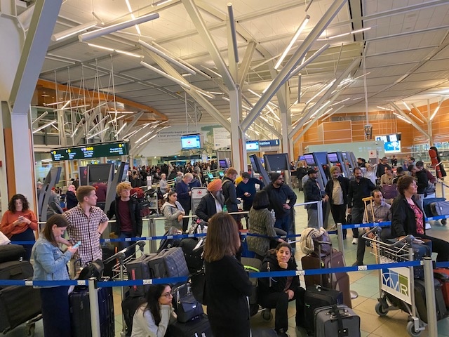 Frustrated passengers at YVR airport, their flights delayed due to a system failure with Air Canada's check-in system, requiring staff to manually create boarding passes.