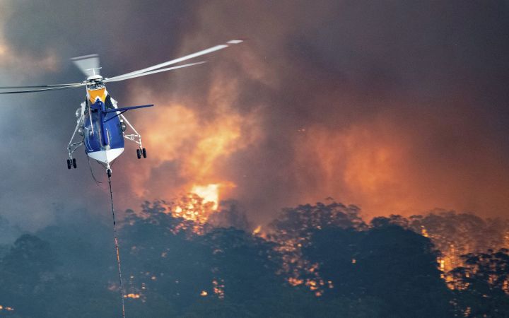 In this Monday, Dec. 30, 2019 photo provided by State Government of Victoria, a helicopter tackles a wildfire in East Gippsland, Victoria state, Australia. Wildfires burning across Australia’s two most-populous states trapped residents of a seaside town in apocalyptic conditions Tuesday, Dec. 31, and were feared to have destroyed many properties and caused fatalities.