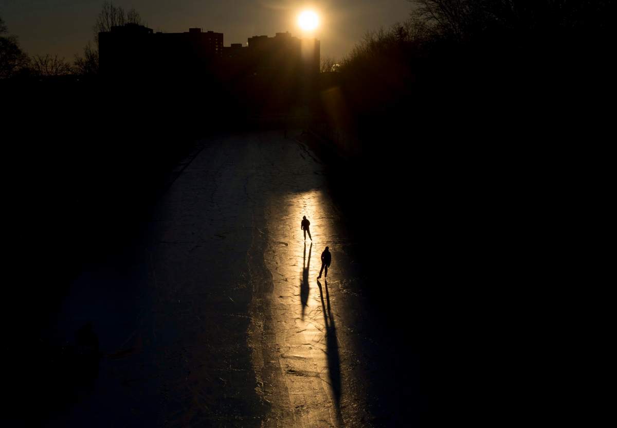 Skaters are silhouetted in a beam of sunlight as they make their way along the Rideau Canal Skateway shortly after dawn on Sunday, Jan. 15, 2017 in Ottawa.