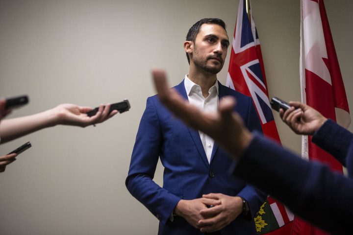 Ontario Education Minister Stephen Lecce talks to reporters in a PC caucus office as protesters join a demonstration organized by the teachers unions outside the Ontario Legislature, in Toronto on Feb. 21, 2020.
