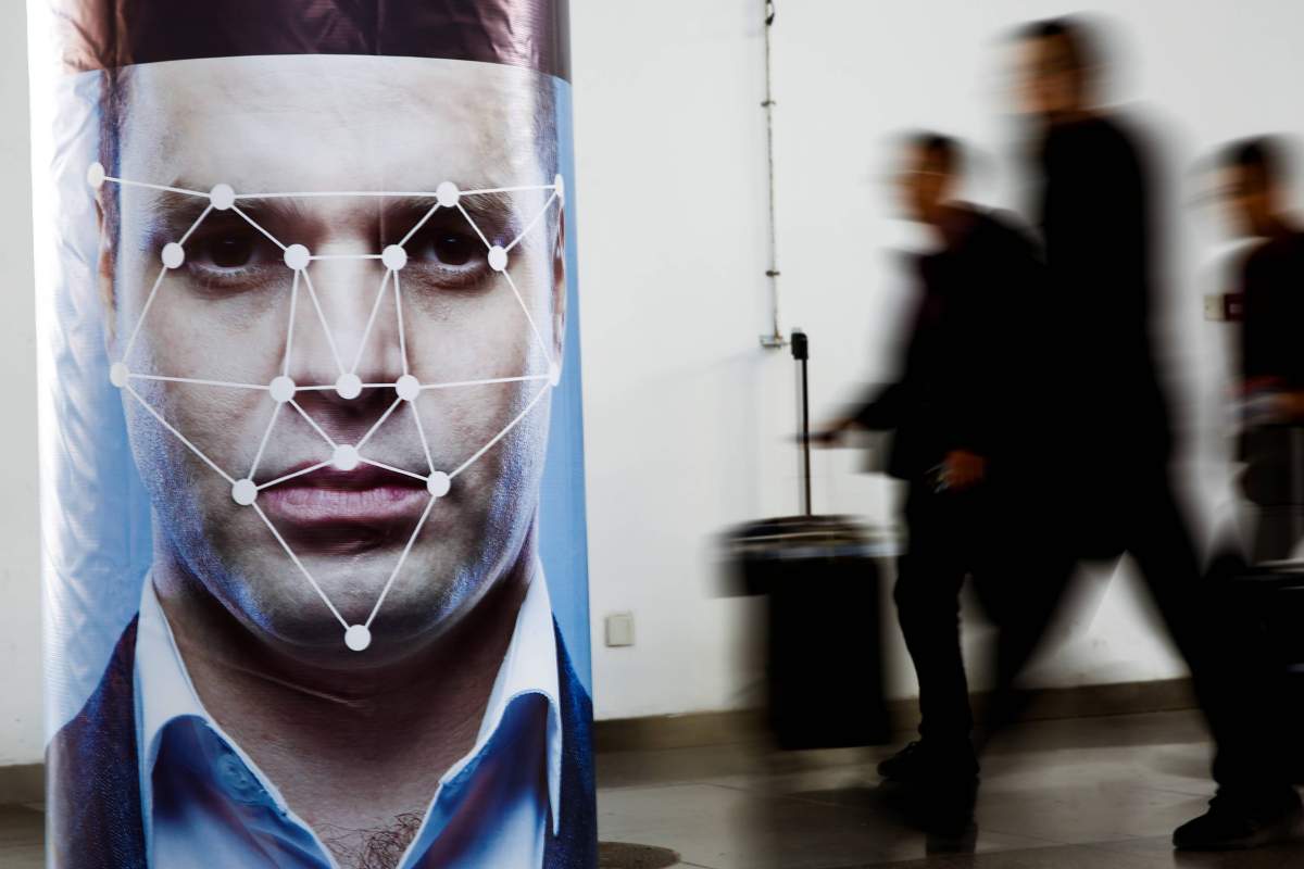 People walk past a poster simulating facial recognition software at the Security China 2018 exhibition in Beijing. 