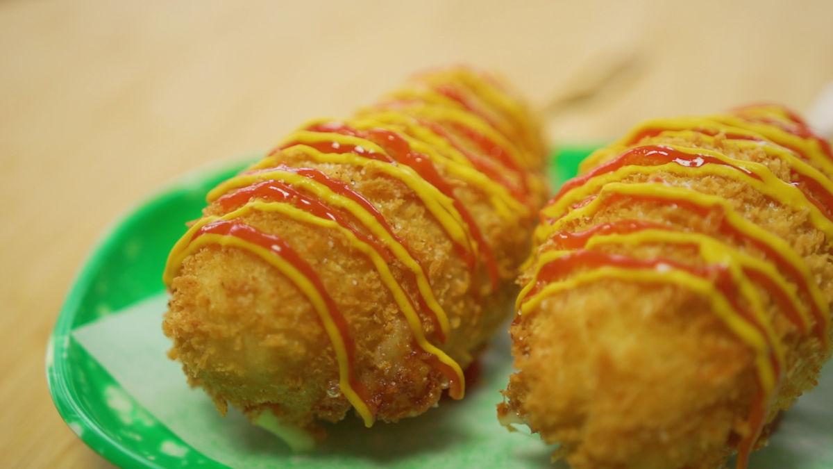 Crispy sugar-coated corndog made with flour and rice flour, filled with half mozzarella and half beef sausage.