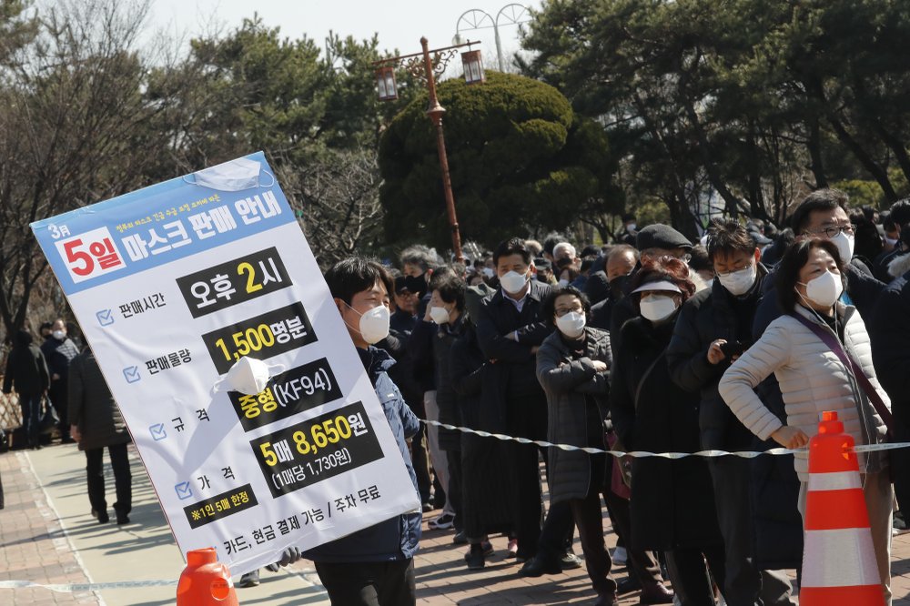 An employee holds a board to give face mask sales informations as people line up to buy face masks to protect themselves from the new coronavirus outside Nonghyup Hanaro Mart in Seoul, South Korea, Thursday, March 5, 2020. The number of infections of the COVID-19 disease spread around the globe. The signs read "Face mask sales informations on March 5, Sale time: PM 2:00 and Sales quantity: 1,500 people.".