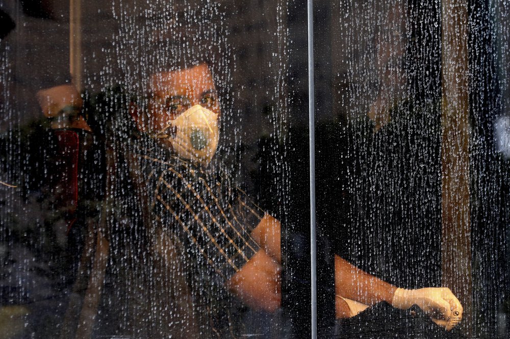 A commuter looks through a water-stained window wearing a mask and gloves to help guard against the Coronavirus, on a public bus in downtown Tehran, Iran, Sunday, Feb. 23, 2020. Iran's health ministry raised Sunday the death toll from the new virus to 8 people in the country, amid concerns that clusters there, as well as in Italy and South Korea, could signal a serious new stage in its global spread. 