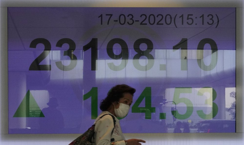 A woman wearing face mask walks past a bank electronic board showing the Hong Kong share index at Hong Kong Stock Exchange Tuesday, March. 17, 2020. Shares have reversed early losses in major Asian markets after the U.S. stock market plunged to its worst day in more than three decades. 
