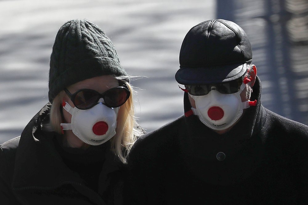 Two people wearing masks walk in Regents Park in London, Monday, March 23, 2020.