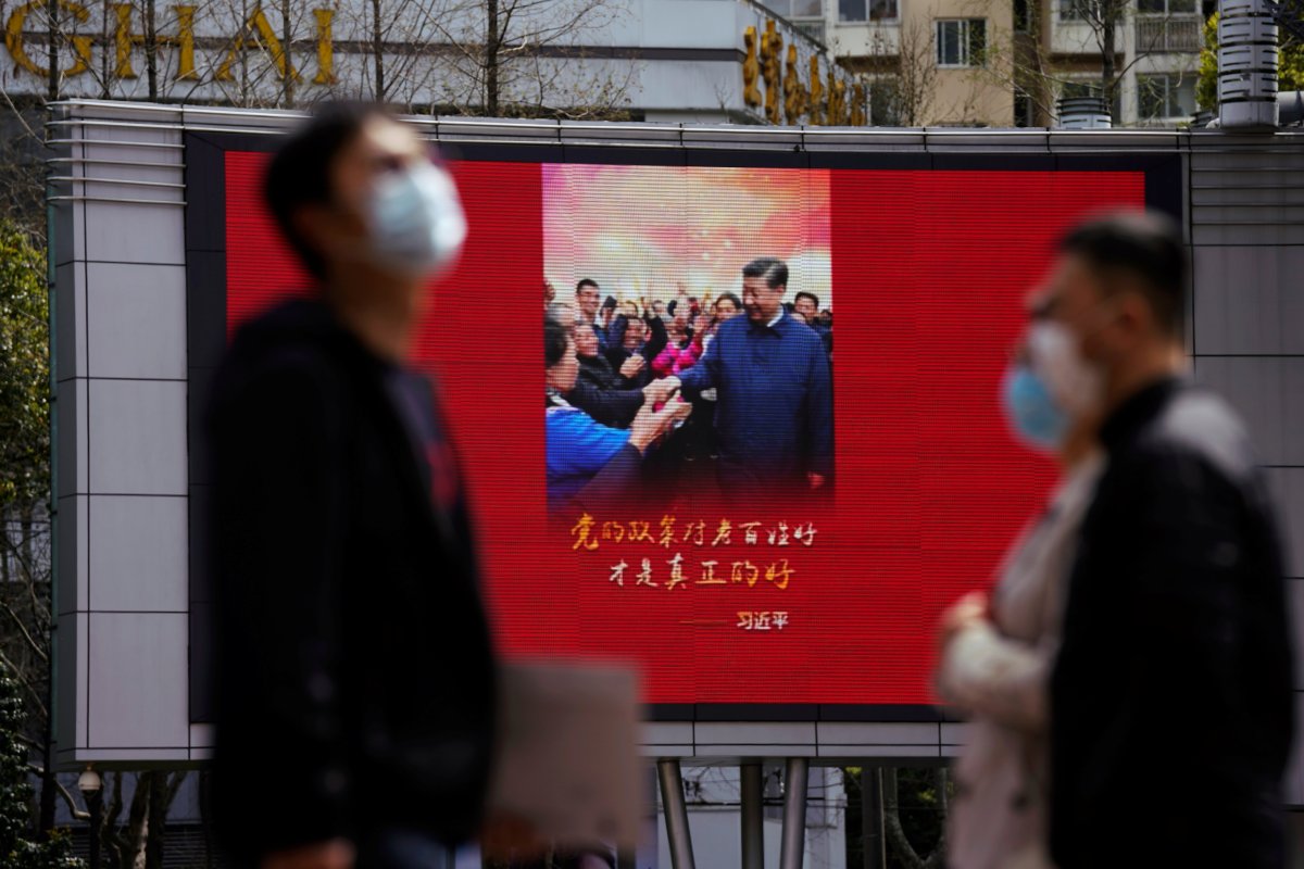 Pedestrians wearing face masks walk past a screen displaying an image of Chinese President Xi Jinping after the city's emergency alert level for coronavirus disease (COVID-19) was downgraded, in Shanghai, China March 23, 2020.  