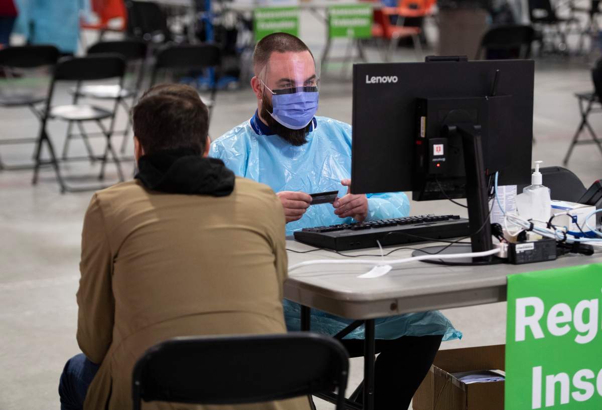 A health care worker looks at the health card of a test patient, a staff member portraying the role of a patient to ensure the assessment systems are working, at a registration table as they prepare for the opening of the COVID-19 Assessment Centre at Brewer Park Arena in Ottawa, during a media tour on Friday, March 13, 2020.