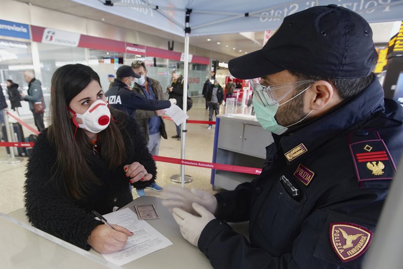 A traveler wears a mask as she fills out a form at a check point set up by border police inside Rome's Termini train station, Tuesday, March 10, 2020. In Italy the government extended a coronavirus containment order previously limited to the country’s north to the rest of the country beginning Tuesday, with soldiers and police enforcing bans. 