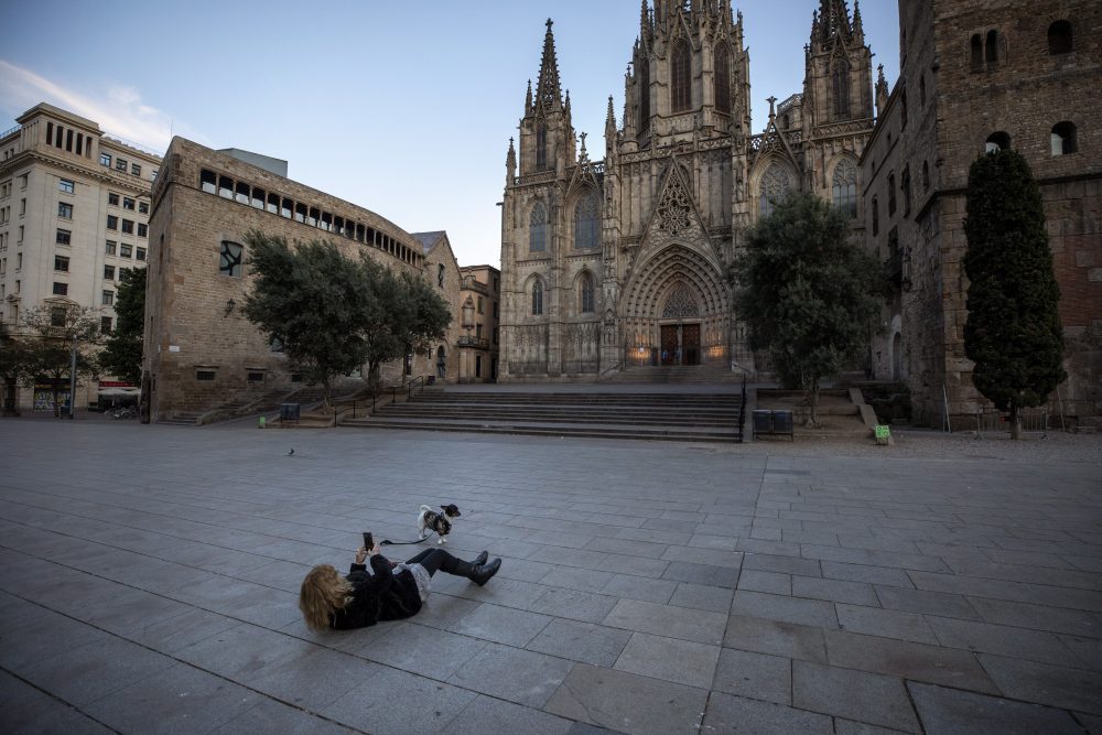 A woman takes a photo of her dog in front of Barcelona’s cathedral, Spain, Sunday, March 15, 2020.