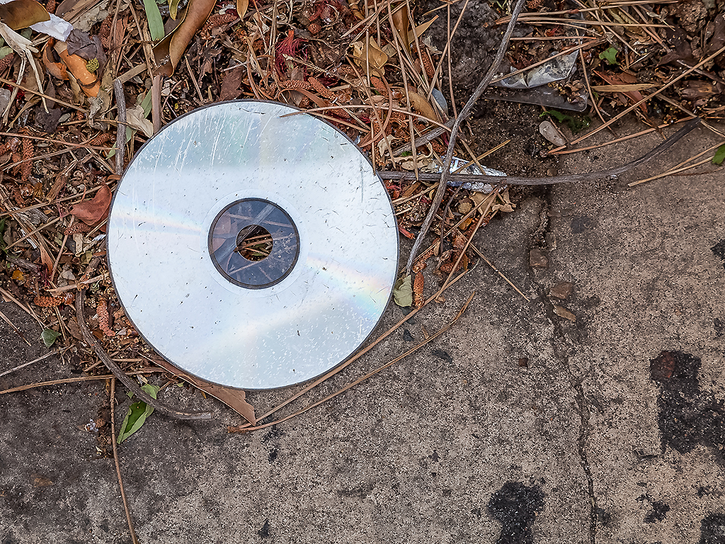 A scratched and dirty CD discarded on the street.
