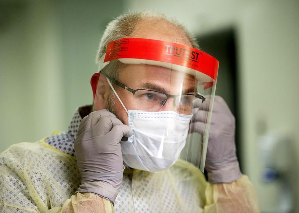 A man demonstrates how to put on a face mask and other protective clothing during a tour of a COVID-19 evaluation clinic in Montreal, Tuesday, March 10, 2020.