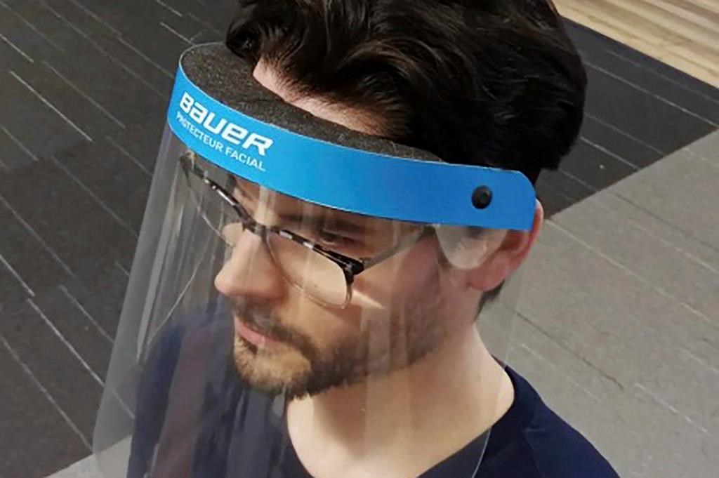 In this March 23, 2020, photo provided by Bauer Hockey Corp., an employee models a medical face shield the hockey equipment manufacturer has begun creating to help those treating the coronavirus pandemic, at Bauer Hockey Corp. in Blainville, Quebec. (Bauer Hockey Corp via AP)