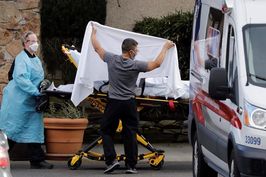 In this Feb. 29, 2020, file photo, a staff member blocks the view as a person is taken by a stretcher to a waiting ambulance from a nursing facility where more than 50 people are sick and being tested for the COVID-19 virus, in Kirkland, Wash.