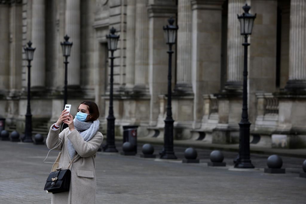 A tourist wearing a mask makes a selfie outside the Louvre museum Friday, Feb. 28, 2020 in Paris.
