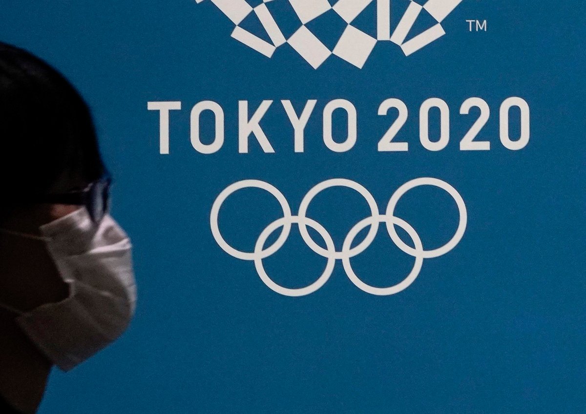 A pedestrian wearing a mask walks past the emblem of the Tokyo Olympic Games in Tokyo, Japan, March 23, 2020.