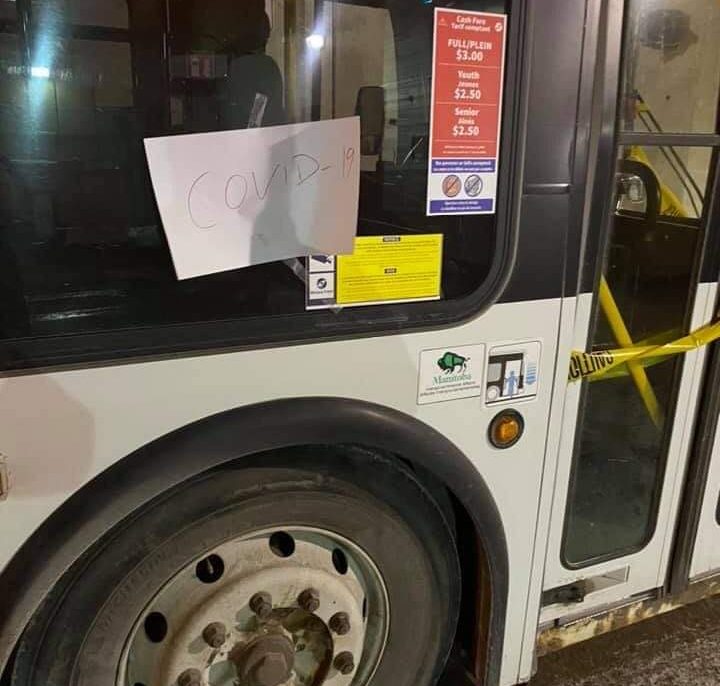 A handwritten sign scrawled with “COVID-19” on a Winnipeg Transit bus.