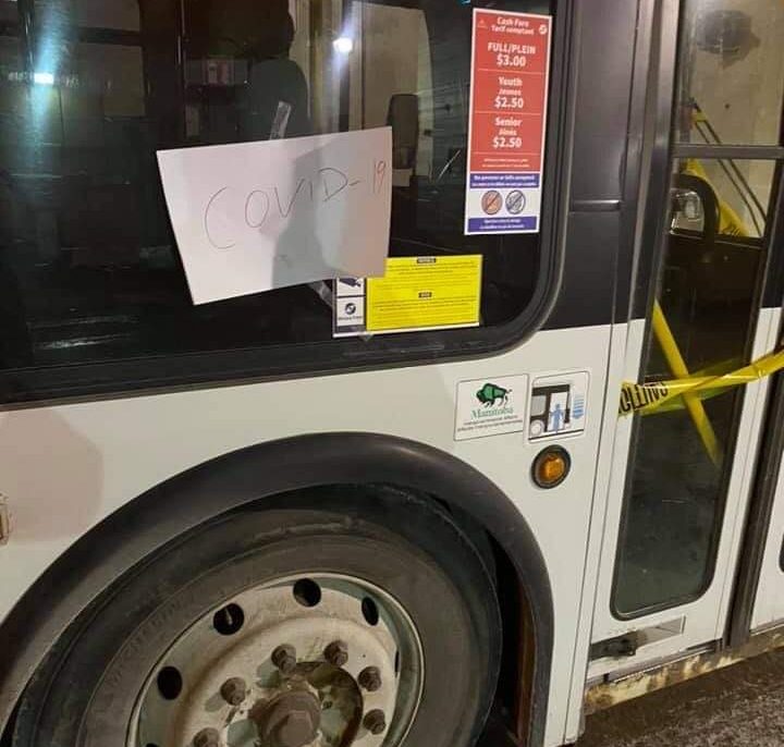 A handwritten sign scrawled with 'COVID-19' on a Winnipeg Transit bus.