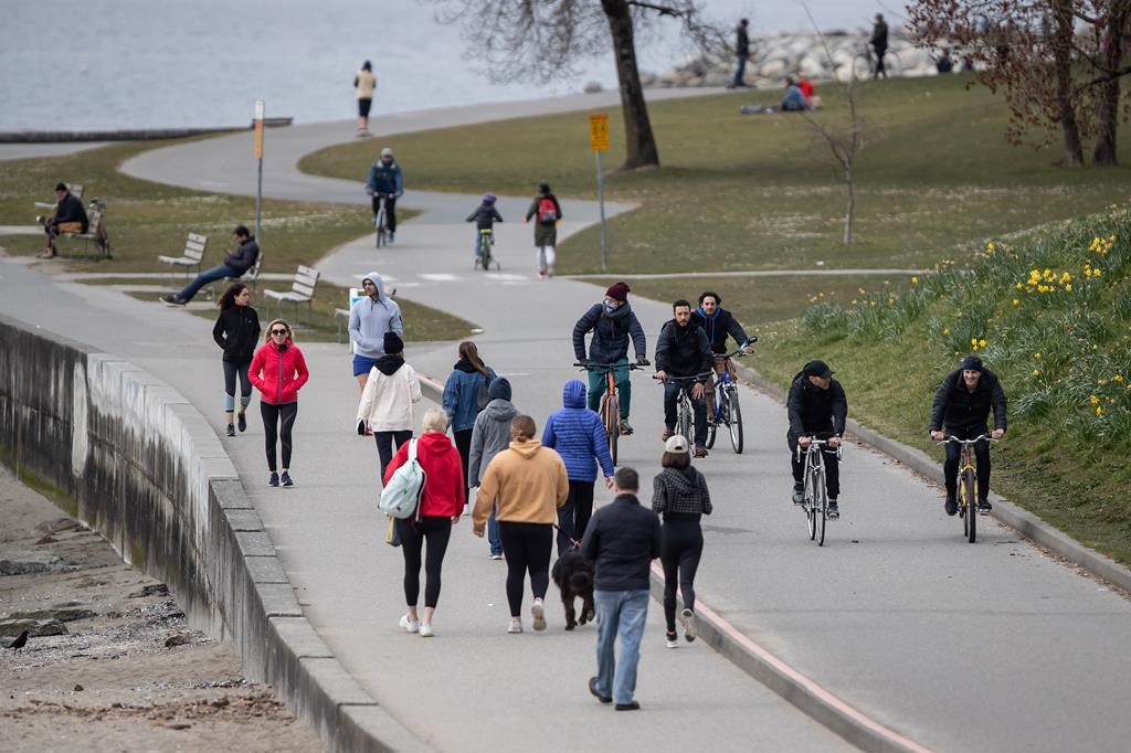 People walk and cycle on the seawall between English Bay and Sunset Beach, in Vancouver, on Sunday, March 22, 2020. 