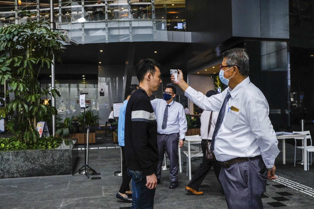 In this March 16, 2020, photo, a man scans a visitor's forehead to check his temperature before entering the Asia Square Tower in Singapore. As the virus outbreak spreads ever further, it's becoming clear that some strategies are more likely to succeed in containing it: pro-active efforts to track down and isolate cases, access to basic, affordable public health and clear, reassuring messaging from leaders. (AP Photo/Ee Ming Toh)
.