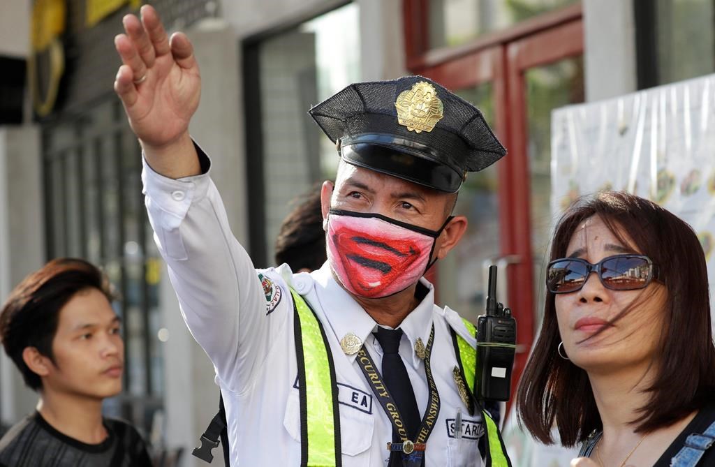 A security guard wearing a protective mask assists a woman in Manila, Philippines Friday, March 13, 2020. Many people adjusted their travel plans ahead of a government suspension of domestic travel to and from metropolitan Manila. Philippine President Rodrigo Duterte also authorized sweeping quarantines in the crowded capital to fight the new coronavirus. For most people, the new coronavirus causes only mild or moderate symptoms. For some it can cause more severe illness. (AP Photo/Aaron Favila).