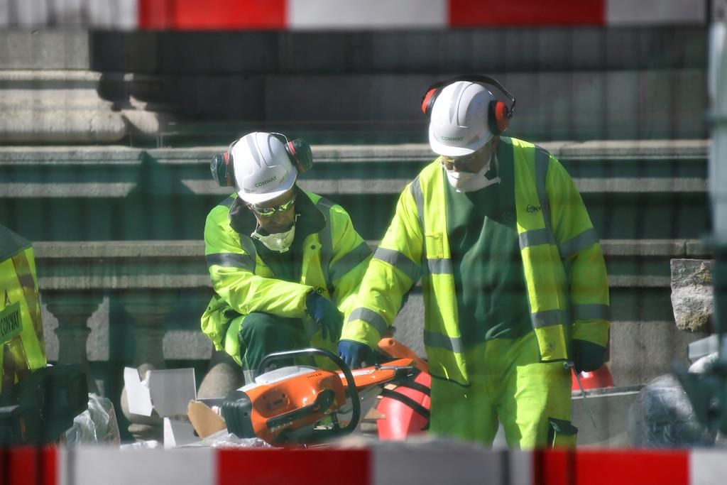Construction workers wearing face masks seen through safety fencing.