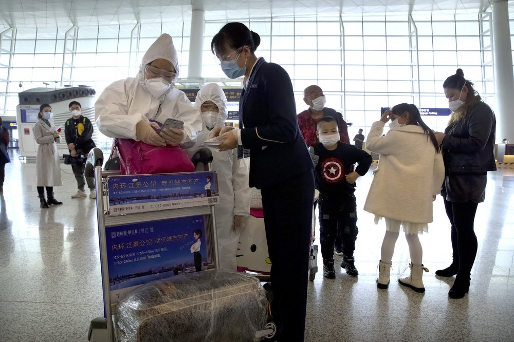 A worker assists travelers wearing face masks and suits to protect against the spread of new coronavirus at Wuhan Tianhe International Airport in Wuhan in central China's Hubei Province, Wednesday, April 8, 2020. Within hours of China lifting an 11-week lockdown on the central city of Wuhan early Wednesday, tens of thousands people had left the city by train and plane alone, according to local media reports.