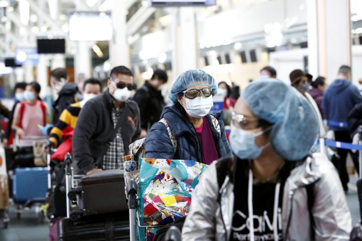 People wearing face masks and goggles wait to check in for an international flight at the Vancouver International Airport on March 16, 2020.