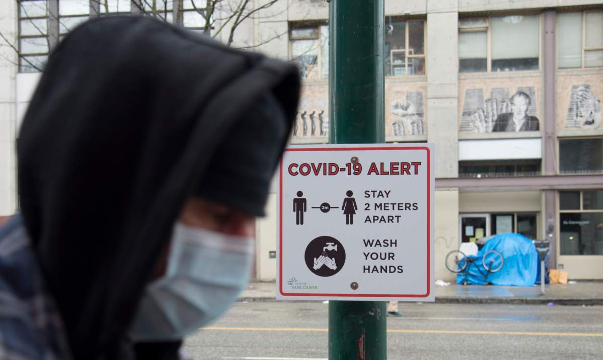 A man walks past a COVID-19 alert sign in Vancouver's downtown eastside Thursday, March 26, 2020. The large amount of homeless living on the streets in the DTES and lack of social distancing may result in a easy spread of COVID-19. 
