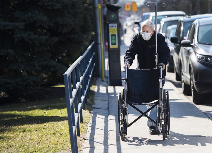 An elderly man wears a mask while returning a wheel chair to the hospital in Toronto on Friday, March 27, 2020.