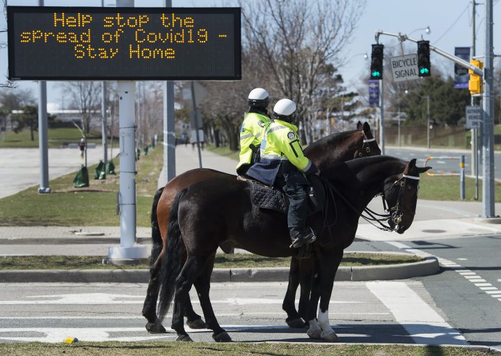 Toronto police officers stop at a red light as they patrol on their service horses in Toronto on Thursday, April 2, 2020. 