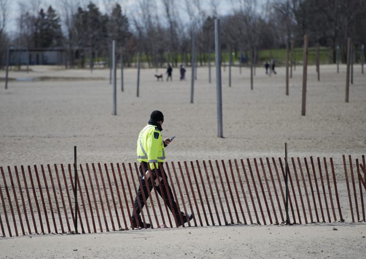 A City of Toronto bylaw officer walks on Woodbine Beach with his ticket book making sure people are practising physical distancing in Toronto on Friday, April 10, 2020. 