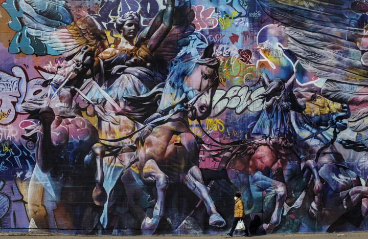 A person carrying groceries and wearing a mask walks past a mural in Edmonton during the COVID-19 pandemic on Saturday, April 11, 2020.