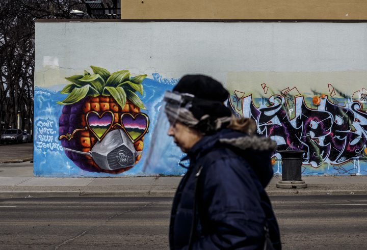 A person wearing a protective face shield walks past a mural in Edmonton, Alta., on Wednesday April 15, 2020, during the COVID-19 pandemic.