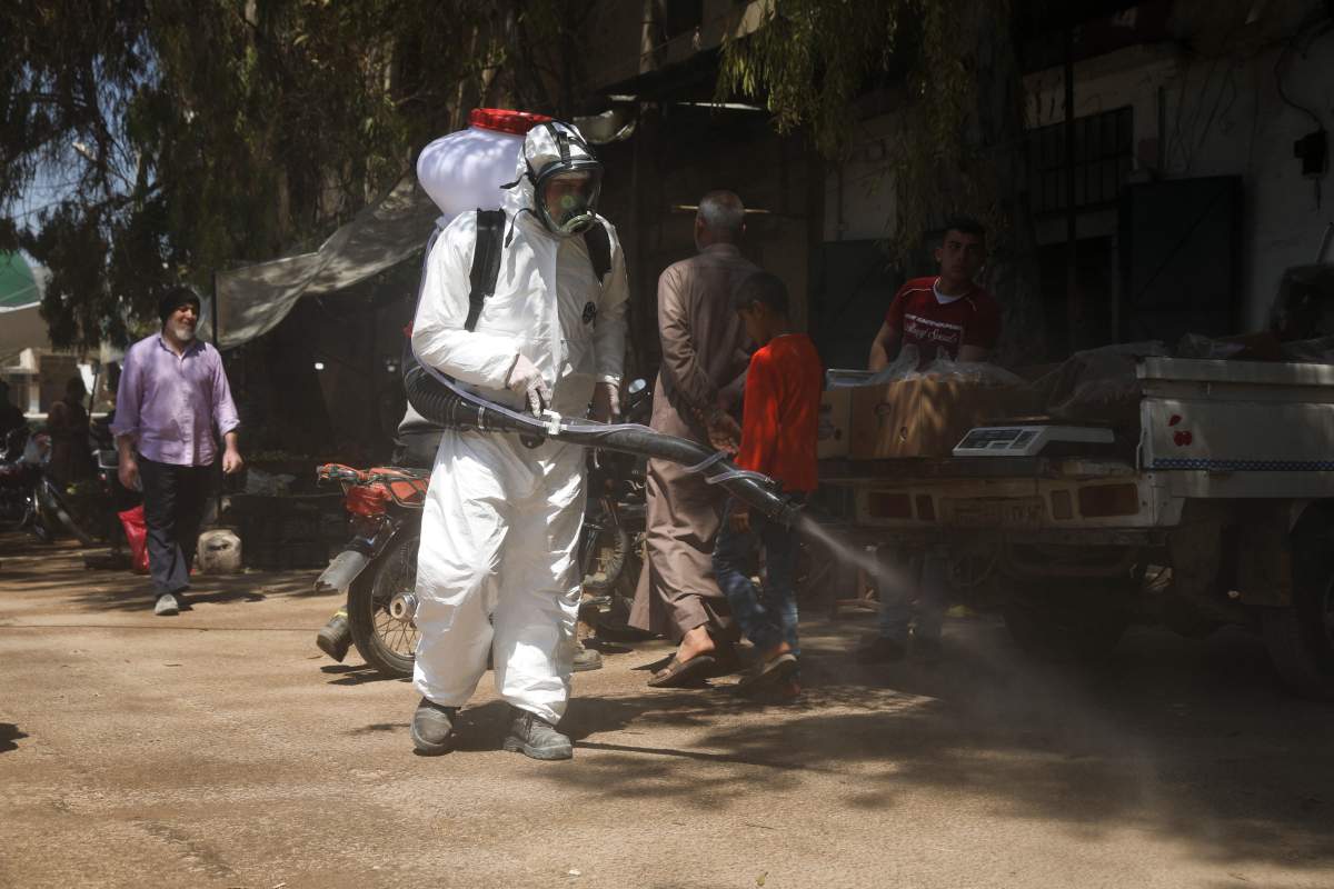 FILE - In this Tuesday, April 14, 2020 file photo, a member of a non-governmental aid organization spray disinfectant as a preventive measure for coronavirus in the town of Armnaz, Idlib province, Syria.