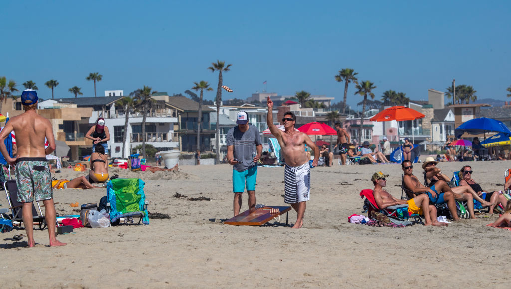 People play a beanbag toss game as they join thousands of beachgoers enjoying a warm, sunny day at the beach amid state-mandated stay-at-home and social-distancing orders to stave off the coronavirus pandemic in Newport Beach, Calif., on April 25, 2020.