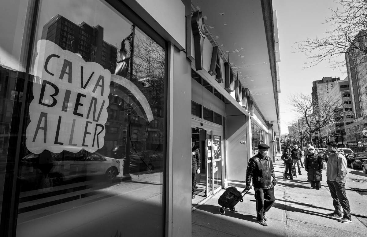 A man wearing a surgical mask leaves an Adonis supermarket on Ste-Catherine Street, Saturday April 4, 2020, as other clients wait in line to enter. To prevent crowding inside stores, customers to wait outside to be called in. Phil Carpenter/Global News