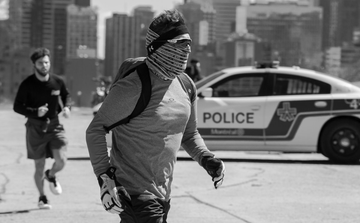 A runner, wth his face and eyes covered, runs past a Montreal police car in Mont Royal park, Saturday April 4, 2020.  Though some medical authorities say that face coverings can help to prevent the coronavirus spread, leaders in Quebec caution that they must not replace physical distancing and hand-washing.