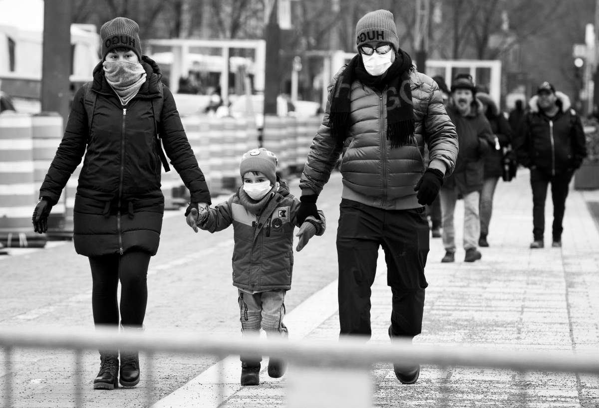 Two adults and a child, all wearing masks, walk towards a COVID-19 screening site in the Quartier des Festivals, Monday March 23, 2020. Phil Carpenter/Global News