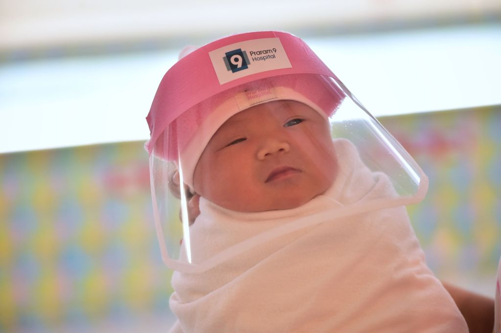 This photo taken through a glass window at a maternity ward shows a newborn baby wearing a face shield in an effort to halt the spread of the COVID-19 coronavirus at Praram 9 Hospital in Bangkok, Thailand on April 9, 2020.