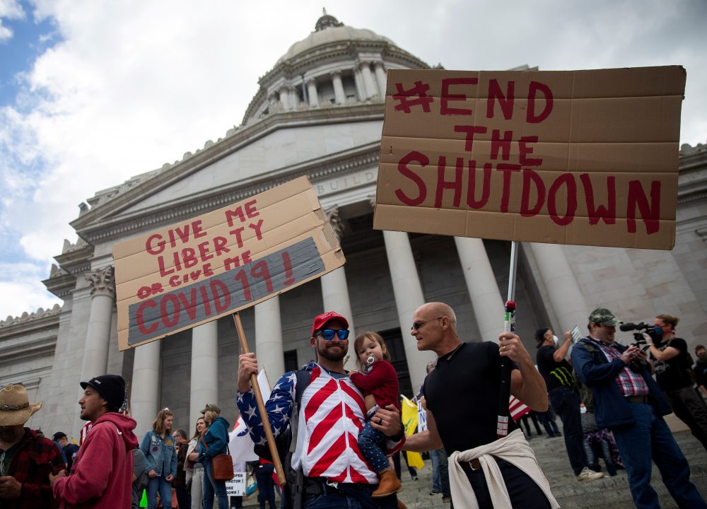 Two men hold signs as they protest against the state’s extended stay-at-home order to help slow the spread of the coronavirus disease (COVID-19) as hundreds gather to demonstrate at the Capitol building in Olympia, Wash., on April 19.