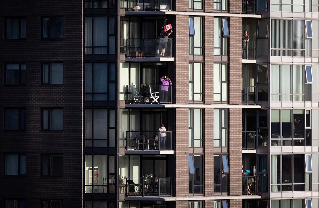 A man waves a flag as others applaud and make noise on condo balconies during the nightly 7 p.m. salute to health-care workers, in Vancouver, on Friday, April 10, 2020.