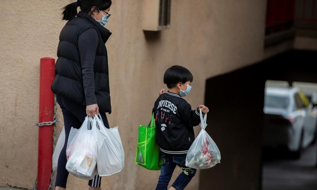 FILE - In this April 2, 2020 file photo, an adult and a child, both wearing face masks amid the coronavirus outbreak, carry bags in the Chinatown neighborhood of Los Angeles. (AP Photo/Damian Dovarganes, File)