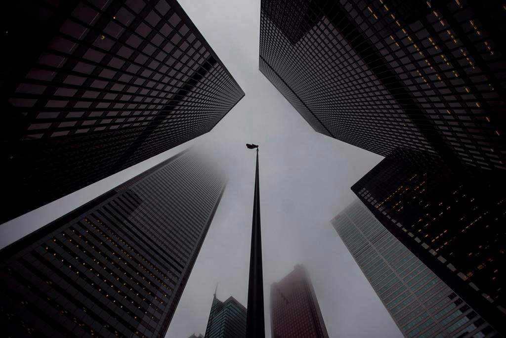 A Canadian flag blows in the wind between bank towers in the heart of the financial district in Toronto on Wednesday, June 27, 2018. Banks are making the switch to virtual-only AGMs this week and next amid COVID-19. THE CANADIAN PRESS/ Tijana Martin.