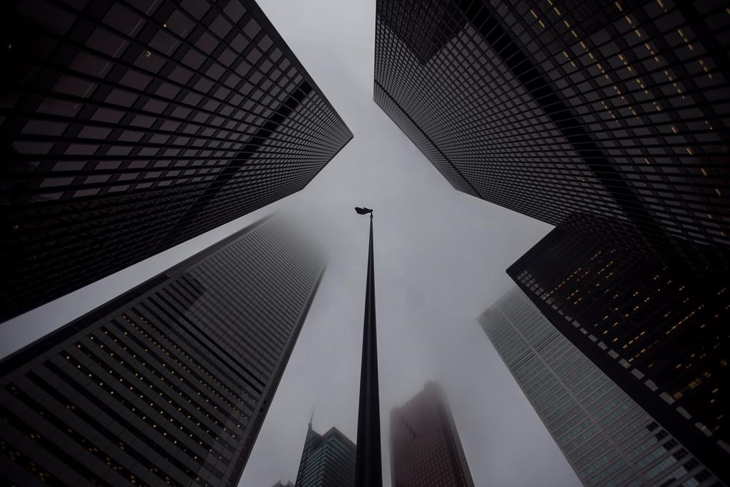 A Canadian flag blows in the wind between bank towers in the heart of the financial district in Toronto on Wednesday, June 27, 2018. Banks are making the switch to virtual-only AGMs this week and next amid COVID-19. THE CANADIAN PRESS/ Tijana Martin.