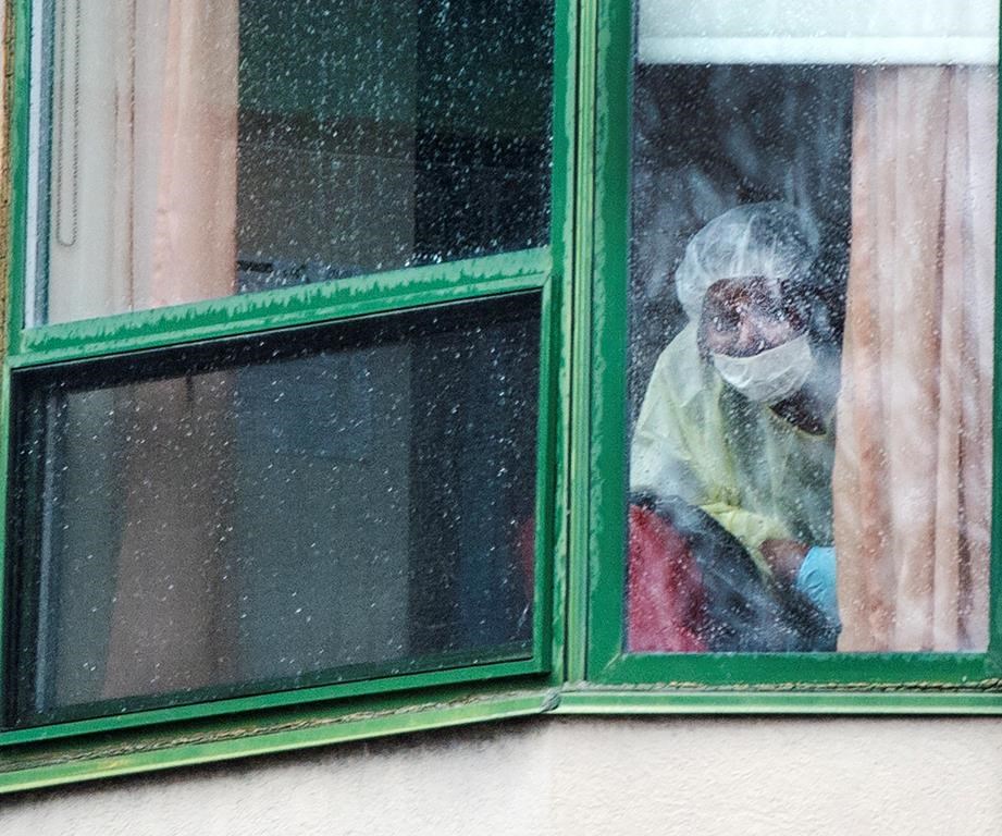 A person wearing protective equipment looks out of a window at the Herron seniors residence Monday April 13, 2020 in Dorval near Montreal's Trudeau airport, where 47 people died.